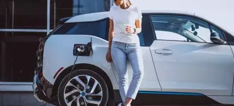 Chica bebiendo café sobre coche eléctrico blanco