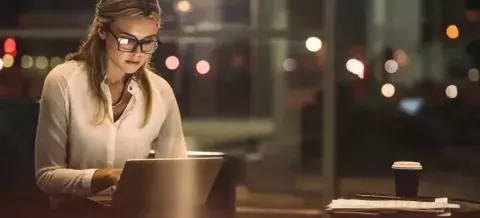 Mujer rubia con gafas trabajando por la noche con un ordenador y un café